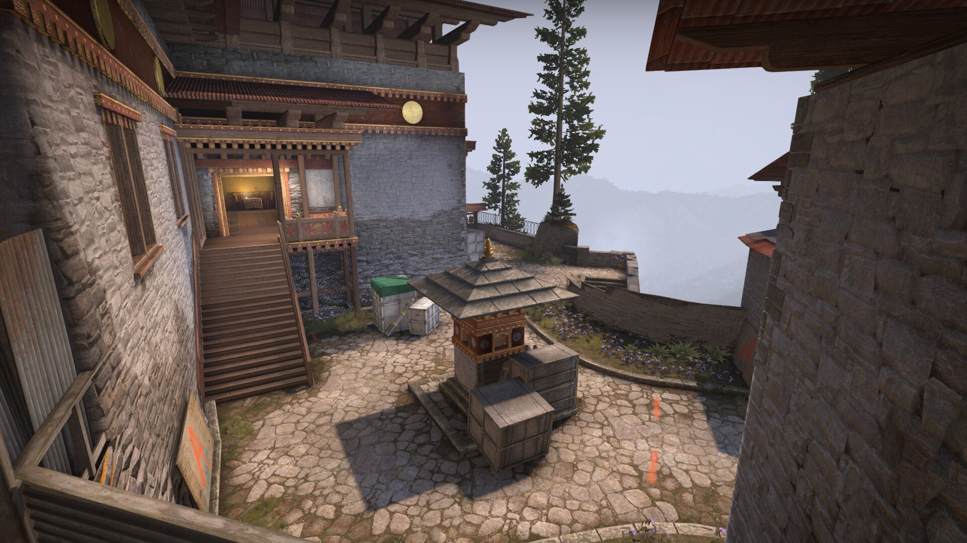 Temple entrance courtyard with a chorten, crates and misty cliffs beyond
