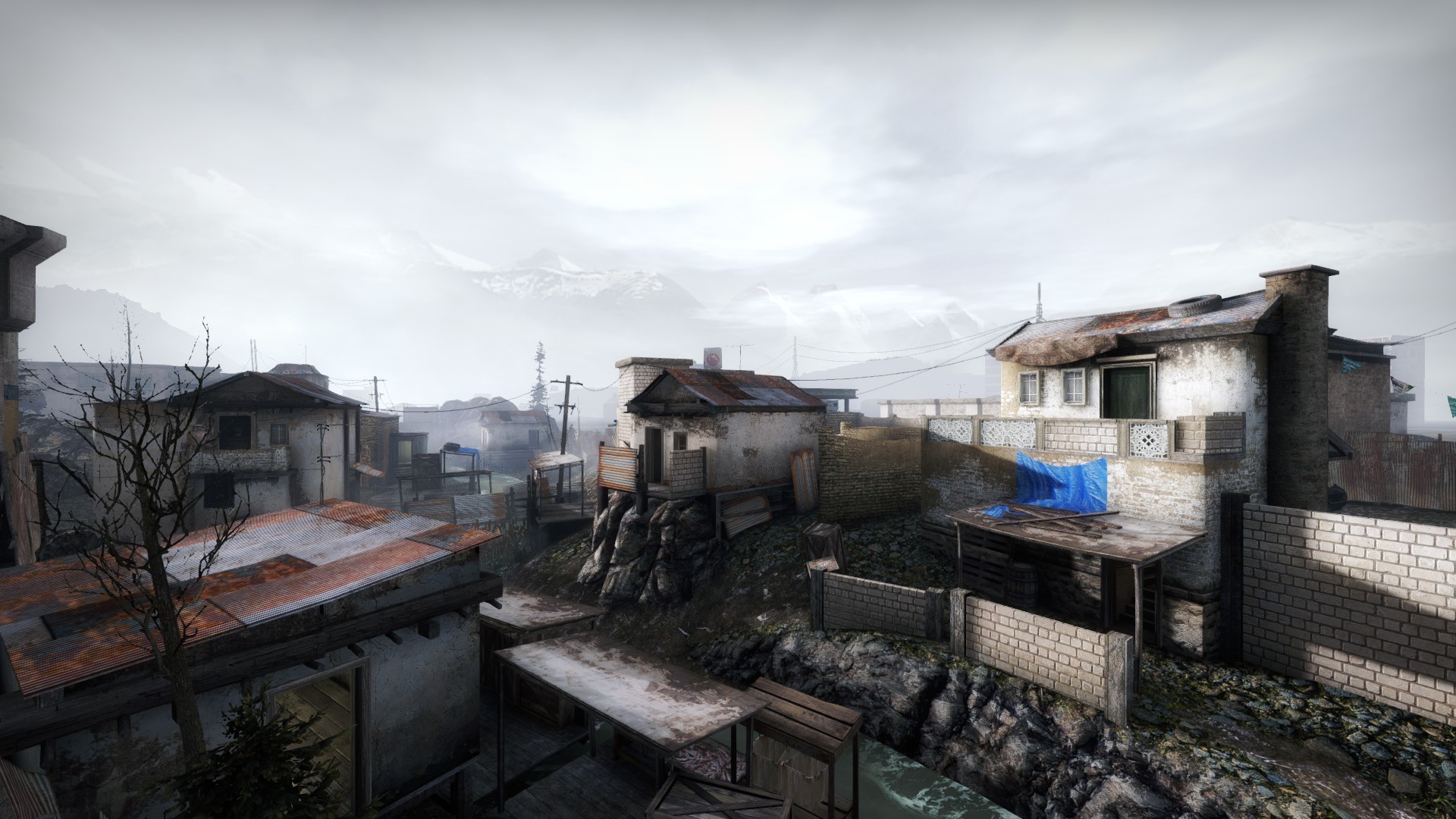 Wide view over a misty mountain village with rusted roofs, brick walls and snowy peaks beyond