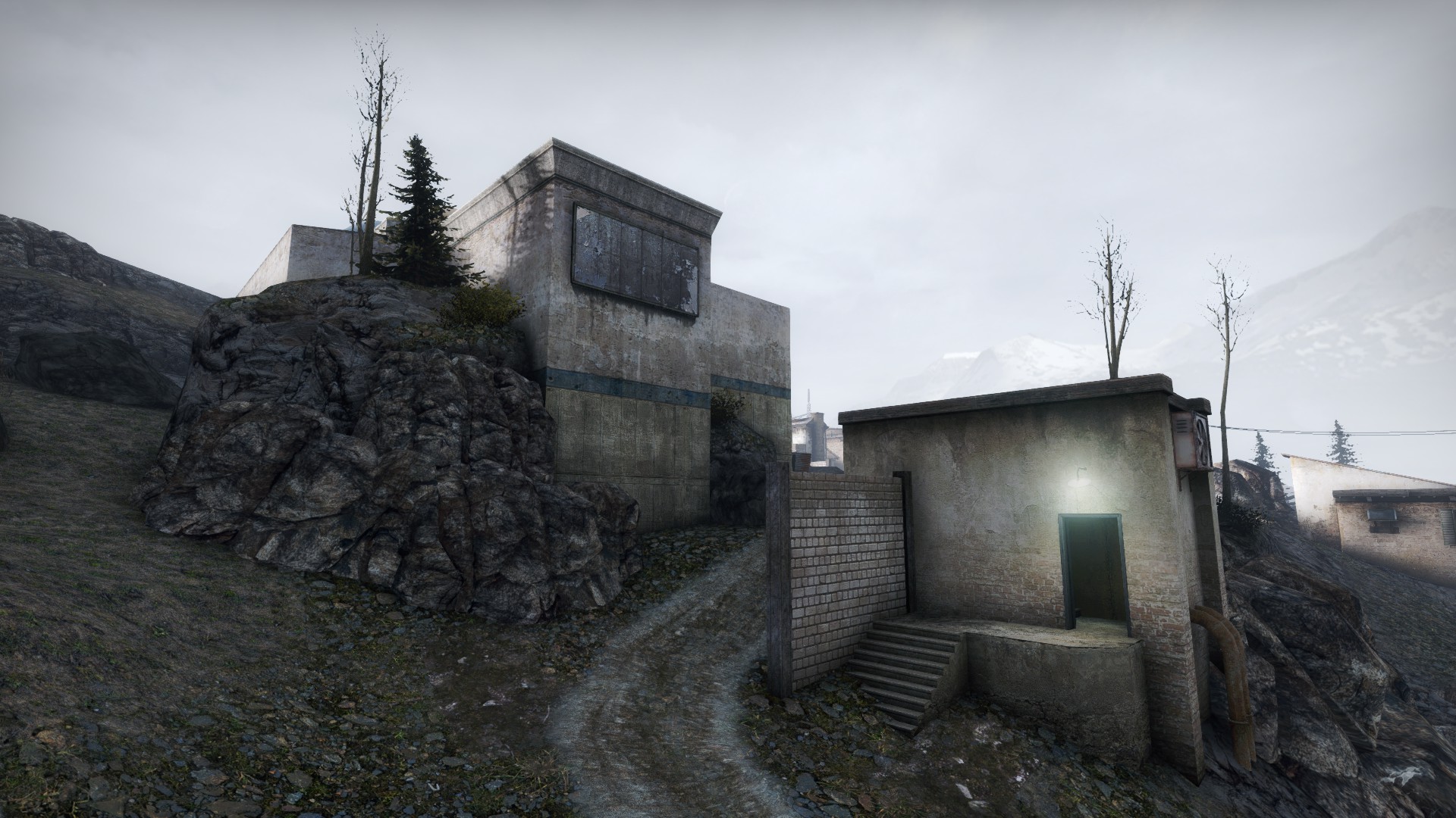 Concrete building perched on a rocky cliff with stairs leading to a lit doorway